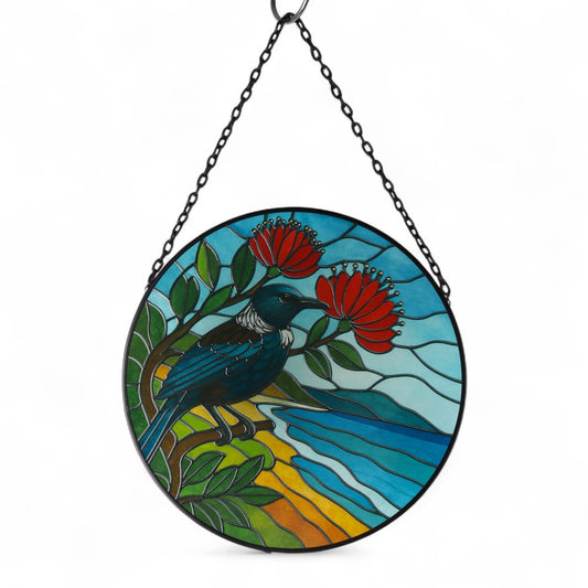 Wall Art - Round Glass - Tui on Pohutukawa Suncatcher
The Tui is a striking native bird of New Zealand, known for its distinctive white throat feathers and melodious song. With iridescent dark plumage and a bold, curved beak, the Tui is a symbol of the country's rich natural heritage. A skilled singer, the Tui can mimic various sounds and is often heard calling in forests and gardens. It plays a key role in pollination and is admired for its beauty, intelligence, and unique vocal abilities. Glass Suncatche
