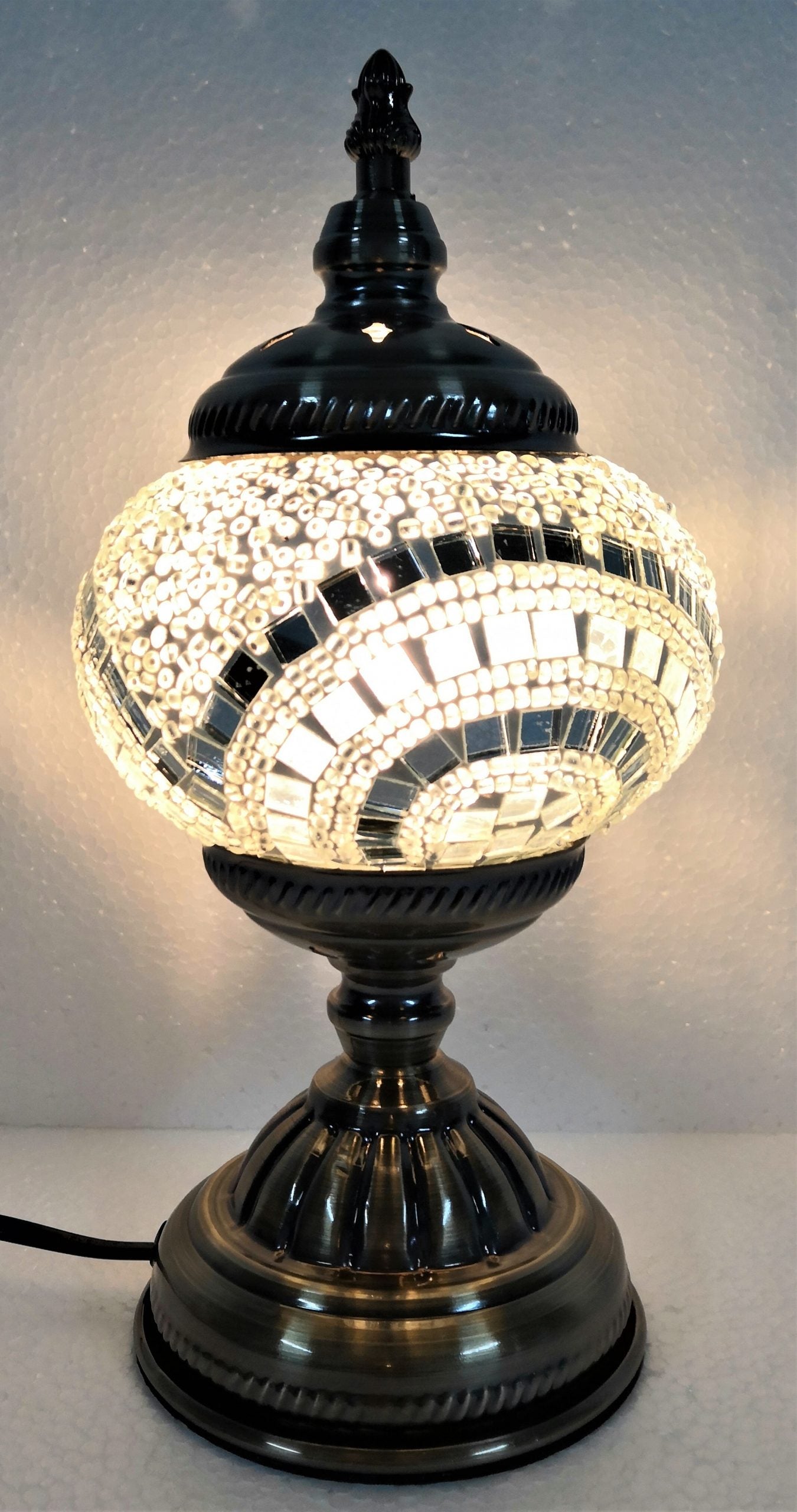 A Turkish mosaic lamp with a white base and a black and white patterned shade, providing a warm light glow.