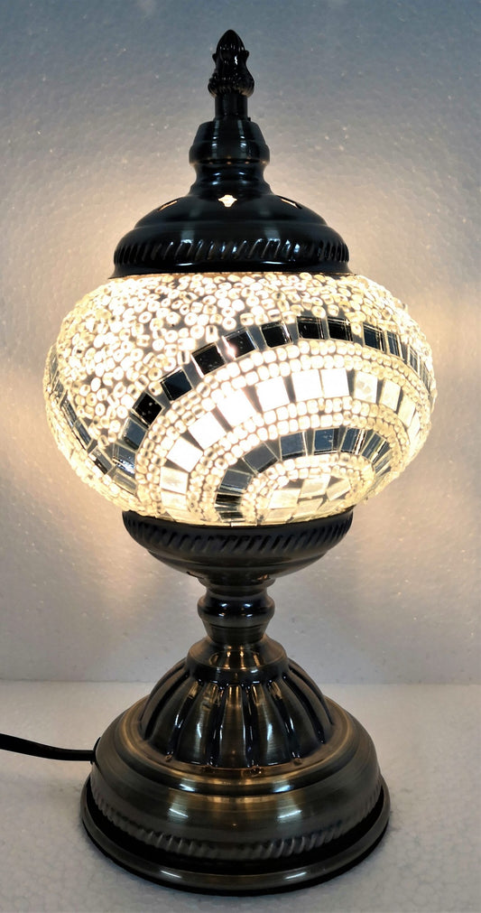 A Turkish mosaic lamp with a white base and a black and white patterned shade, providing a warm light glow.