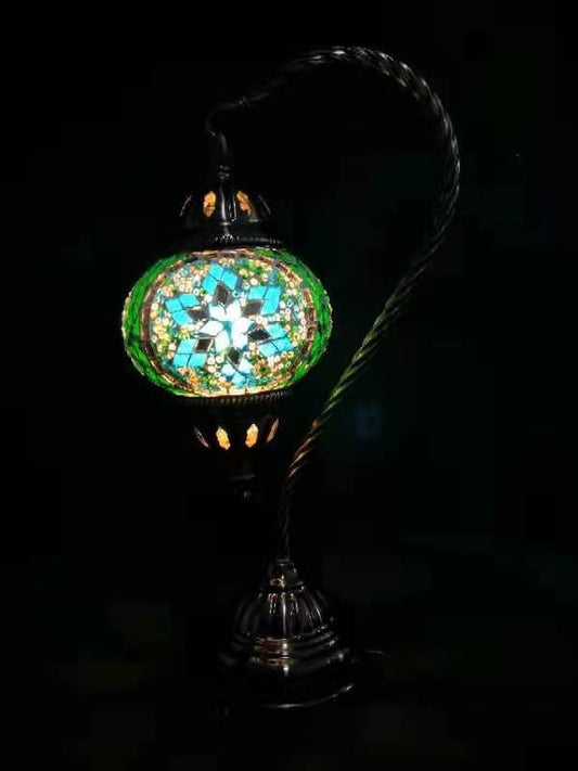 A Turkish mosaic lamp with a swan neck design, featuring multicolored glass tiles, mounted on a metal base and standing against a dark background.
