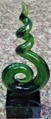 A sculpture of a green kiwi fruit made with glass and placed on a black stand.
