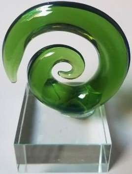 A glass sculpture with a swirling green design, displayed in a clear frame.