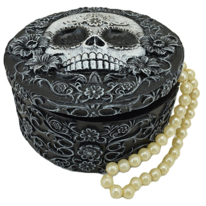 Decorative box with skull design and floral patterns, accompanied by a pearl necklace on a white background.