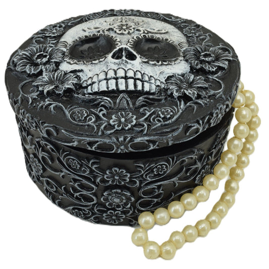Decorative box with skull design and floral patterns, accompanied by a pearl necklace on a white background.