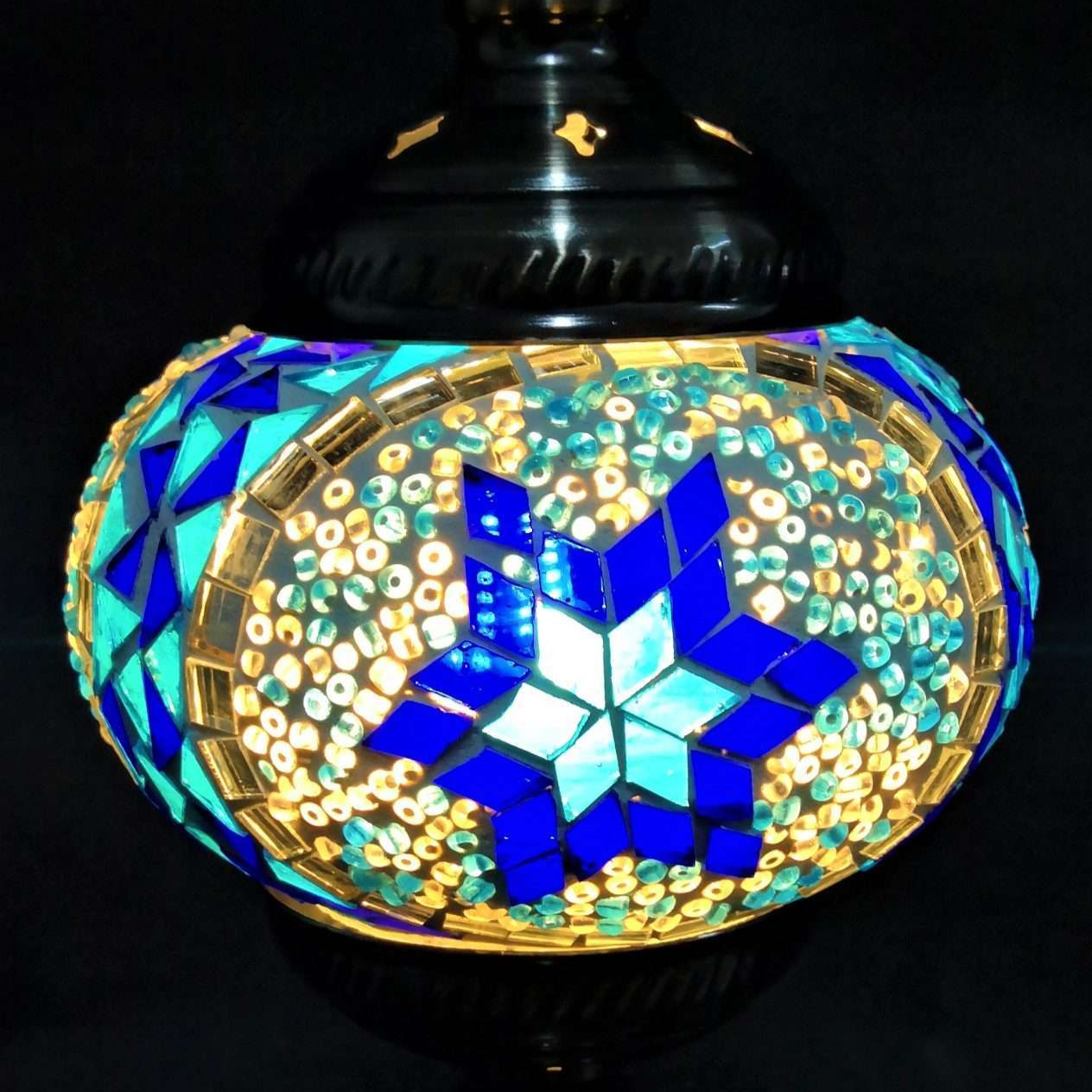 A Turkish mosaic lamp with a multicolored geometric pattern, predominantly blue and gold, mounted on a black iron base with a dark glass shade.