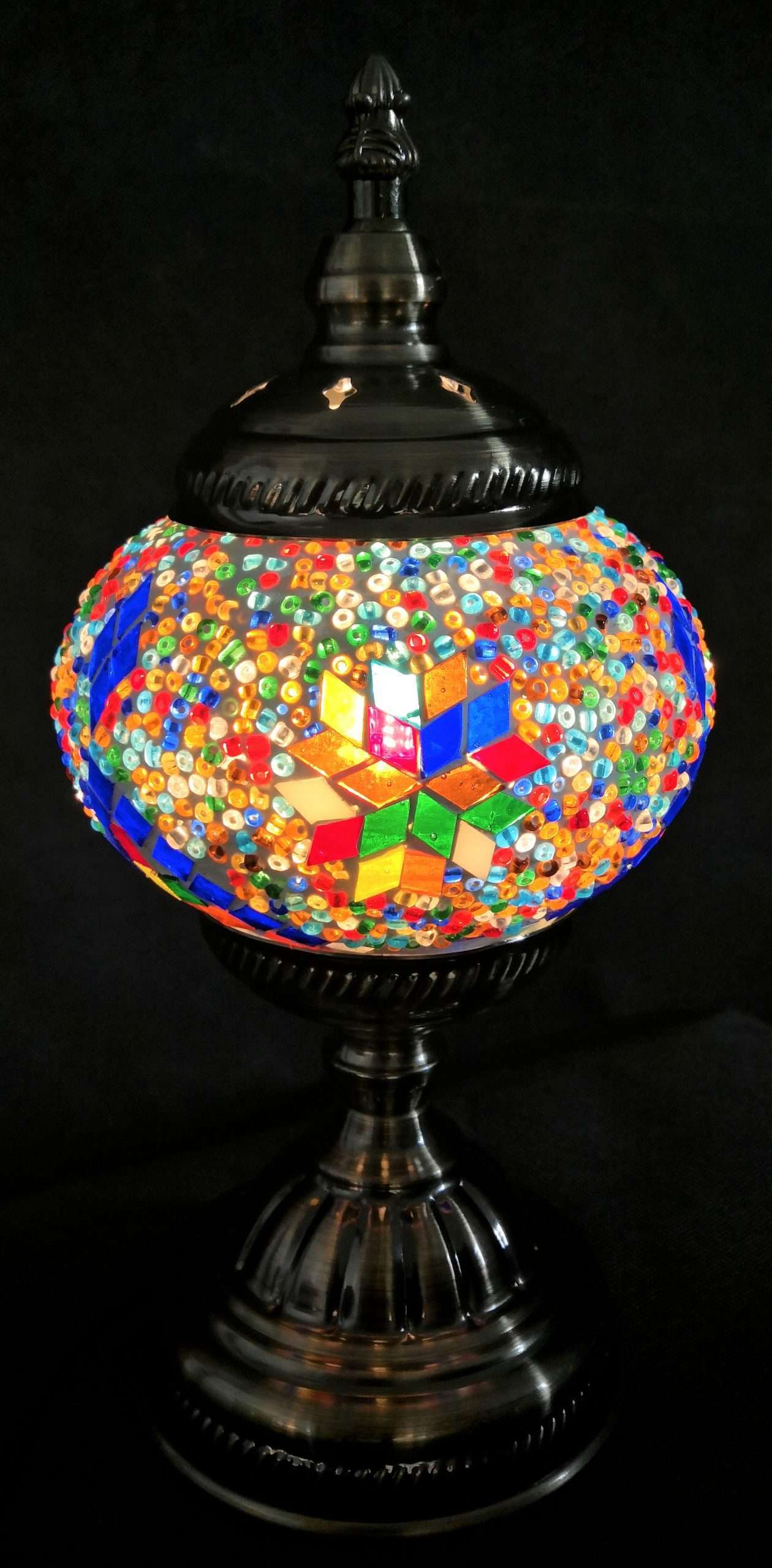 Colorful mosaic table lamp with a black base on a dark background