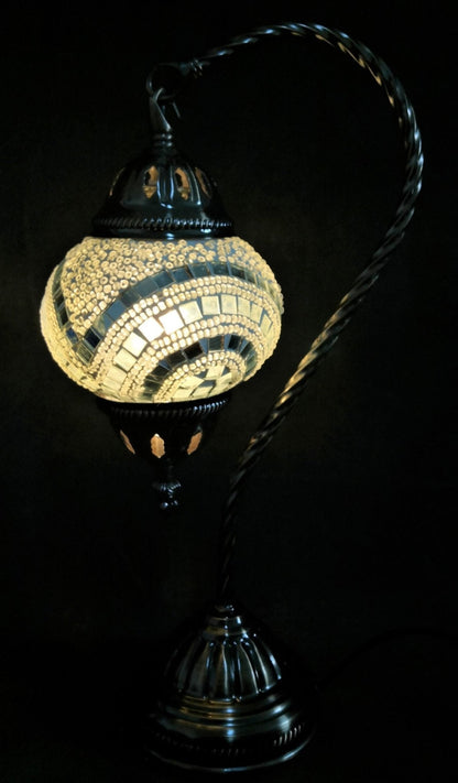 A Turkish mosaic lamp with a swan neck design featuring a white tiled base and a black metal stem, emitting a warm light.